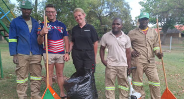 A group of five men and one woman, each holding shovels and trash bags, engaged in a community cleanup effort.