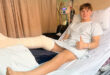 A young man lying in a hospital bed, wearing a cast on his leg, looking contemplative and recovering from an injury.