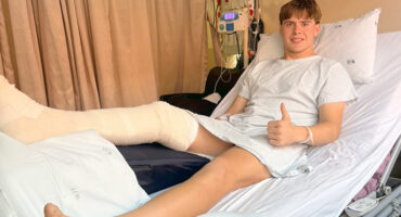 A young man lying in a hospital bed, wearing a cast on his leg, looking contemplative and recovering from an injury.