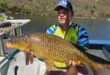 A man proudly holds a large fish while standing on a boat, showcasing his catch of the day.
