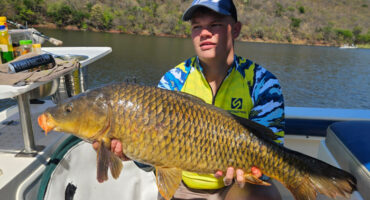 A man proudly holds a large fish while standing on a boat, showcasing his catch of the day.