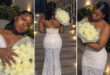 A woman in a white dress stands gracefully, holding a vibrant bouquet of flowers in her hands.