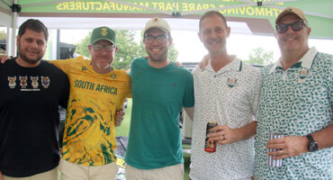Five men smile and pose together at a lively beer tent, surrounded by festive decorations and drinks.