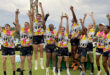 A group of men in yellow and black shirts proudly displaying their trophies in celebration.