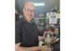 A man with glasses and a beard holds a small statue, smiling as he showcases the intricate details of the figure.