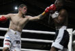 Two boxers engage in a match inside a boxing ring, illuminated by bright lights at night.