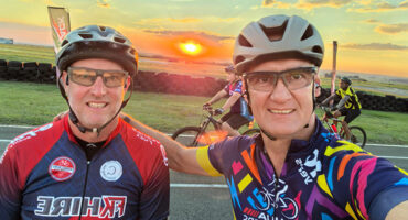 Two men riding bicycles against a backdrop of a vibrant sunset.