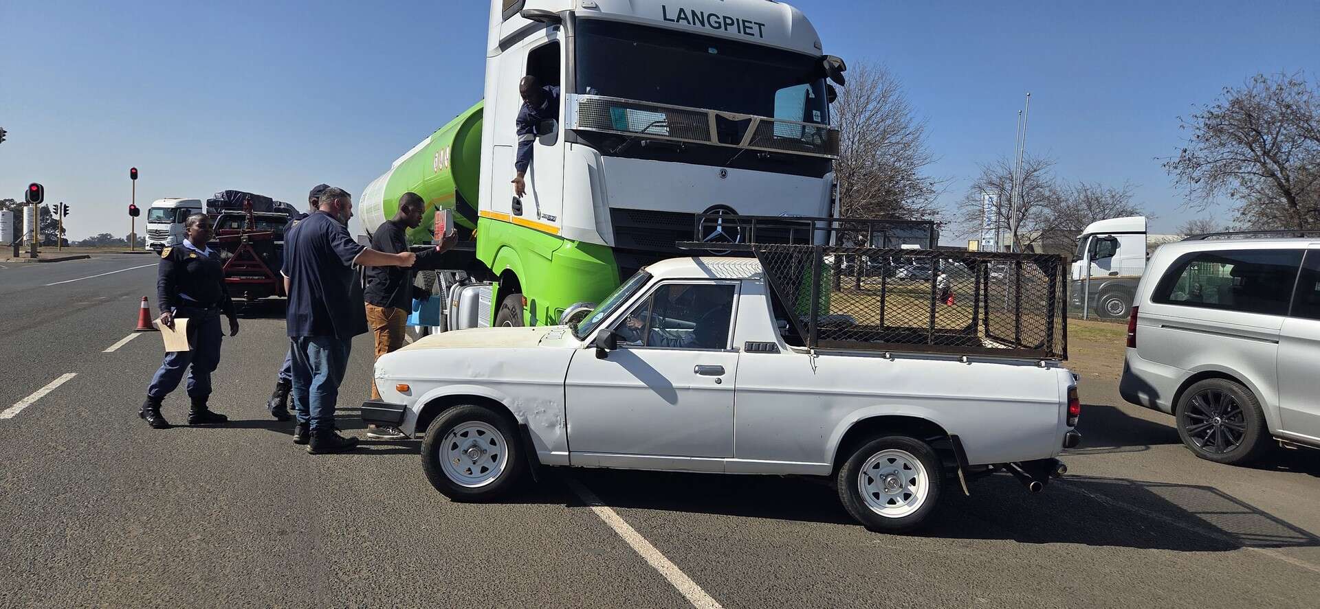 Vooruitsig van ’n Nissan 1400 bakkie met polisie en omstanders wat rondom die voertuig staan na ’n ongeluk naby die N2 en Havenga-kruising in Ermelo.