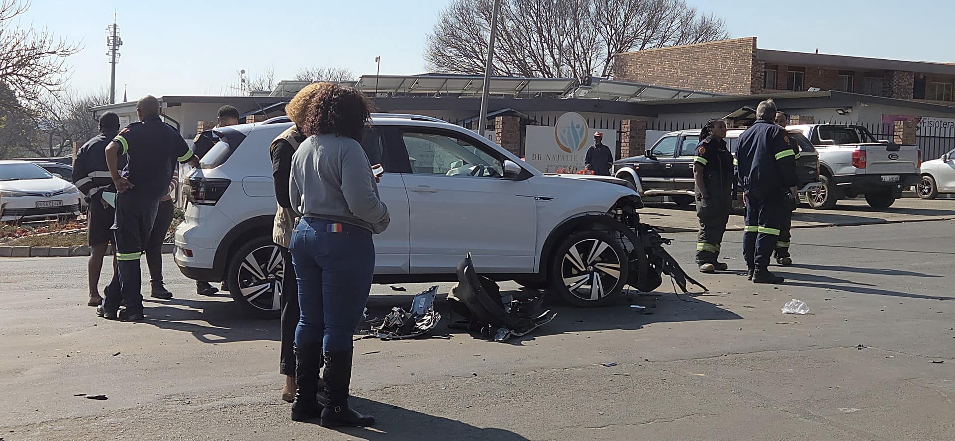 A white car with a heavily damaged front end is at the center of an intersection, surrounded by emergency personnel and bystanders. A smaller circular image in the bottom left shows two white minibus taxis parked on a street. Text at the bottom reads, "Two vehicles collide at intersection" with a "WATCH VIDEO" button next to it.