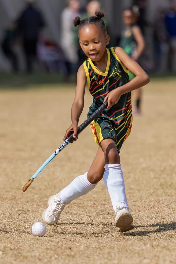 Angeliyah Qila dribbel die hokkiebal vaardig op die veld tydens interskool sportdag.
