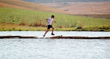 ’n Trail-atleet hardloop oor ’n smal houtwaterbrug tydens die Glen Aggy Trail.