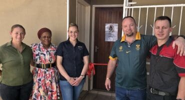 Marthie Botes, Trudy Gasibone, and aspirant knights Theressa van der Walt, JP Robberts, and Bernard Oberholzer standing by the ribbon at CMR Youth Care Centre.
