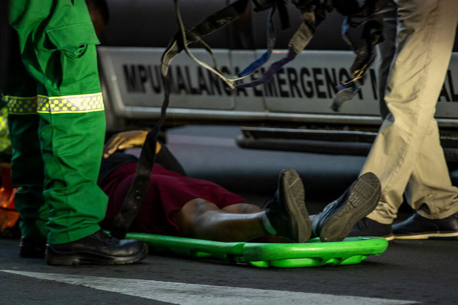 Paramedics attend to an injured woman lying on the ground near the Pick n Pay traffic light in Ermelo, her feet visible as they prepare the stretcher.