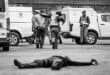 Police officer lies on the ground after being shot during a simulated robbery, while another officer arrests the suspect and escorts him to a police van in Ermelo.