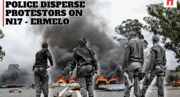 Police disperse protesters on the N17 near Ermelo as vehicles pass while debris and roadblocks are cleared.