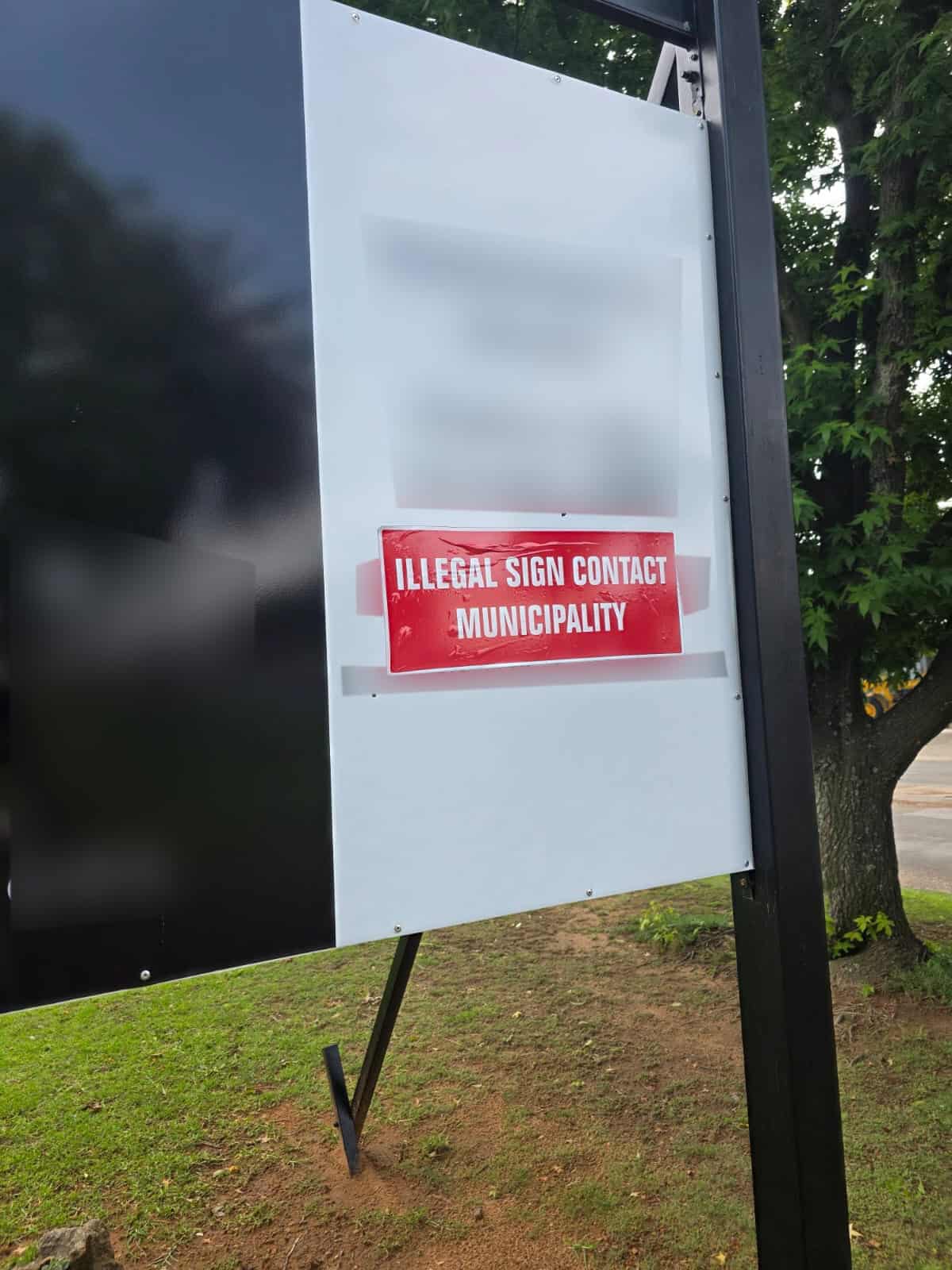 Red sticker on a business sign in Ermelo CBD, placed by the municipality to mark non-compliant signage during a bylaw enforcement operation.