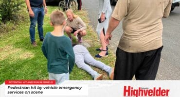 Crowd gathers around a woman injured in De Bruin Street, Ermelo, with emergency responders attending to her.
