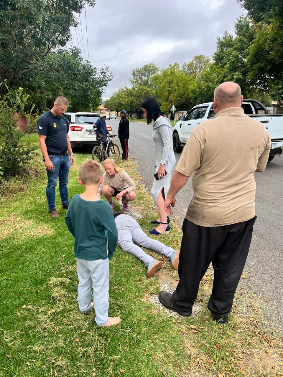 Crowd gathers around a woman injured in De Bruin Street, Ermelo, with emergency responders attending to her.