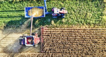 Lugfoto van ’n stroper wat mielies oes en graan in ’n sleepwa aflaai tydens die oesseisoen.