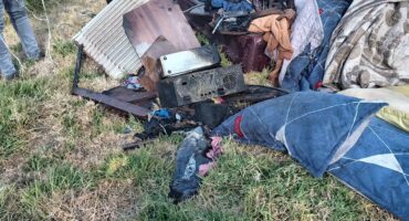 Burnt household items and damaged belongings are scattered outside a fire-damaged home after a destructive blaze.