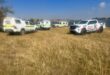 Emergency response vehicles, including SAPS police and a Spartan bakkie, parked on a grassy field next to Douglas Dam in Ermelo during a reported drowning response.