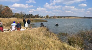 Police divers recovering the body of a woman from Douglas Dam while SAPS and Spartan Security stand on the shoreline
