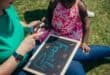 Adult assisting a young child with learning activities outdoors using a chalkboard