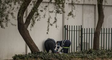 Forensic investigators examine the body of an unidentified man found on a sidewalk behind vegetation near a palisade fence at Oak Centre in Ermelo.