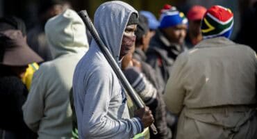 Masked protester holding a baton during a public gathering in Ermelo.