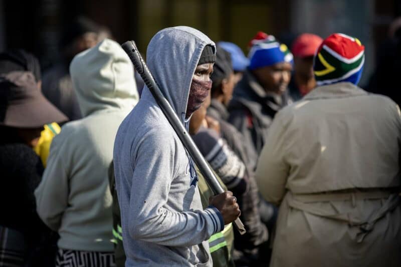 Masked protester holding a baton during a public gathering in Ermelo.