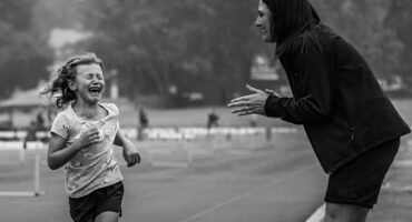 Elsa Winckler runs towards the finish line as Marnel van Niekerk passionately cheers her on from the sidelines during an athletics event.