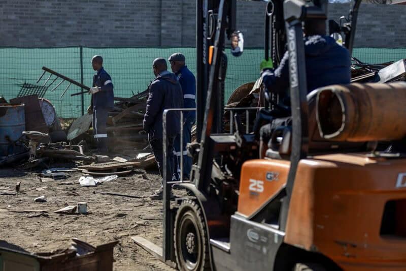 A forklift operator moves scrap metal while police search an Ermelo scrap yard.