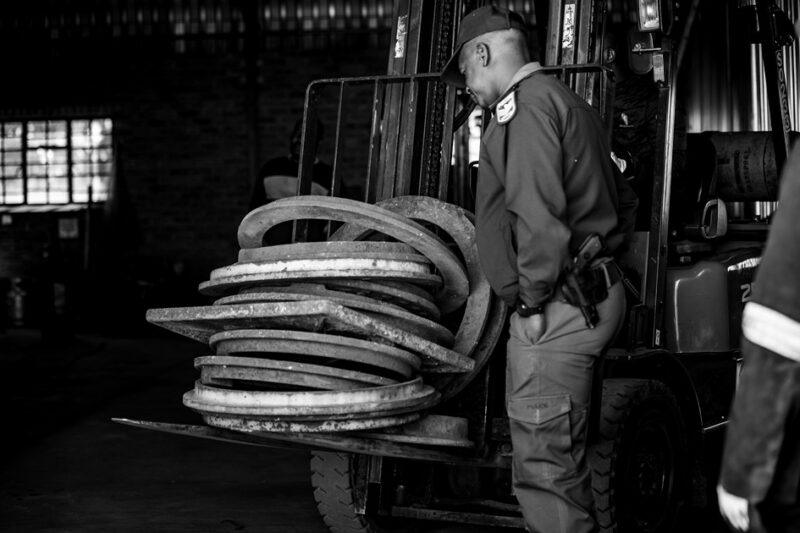 A police officer stands next to a forklift loaded with recovered manhole covers and rings at an Ermelo scrap yard.