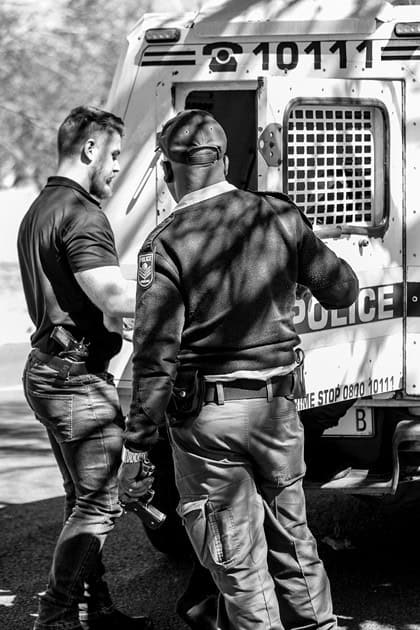 Security officer and police officer place a detained man into a police vehicle.
