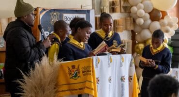 Group of learners reading pages from novels brought to their school by BookHive representatives during a reading activity.