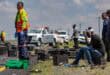 Injured driver sits beside the road with a bandaged head after a bakkie and trailer overturned.