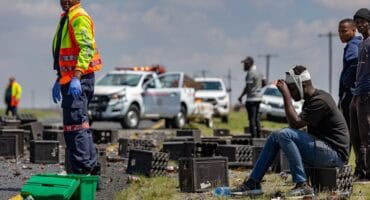 Injured driver sits beside the road with a bandaged head after a bakkie and trailer overturned.