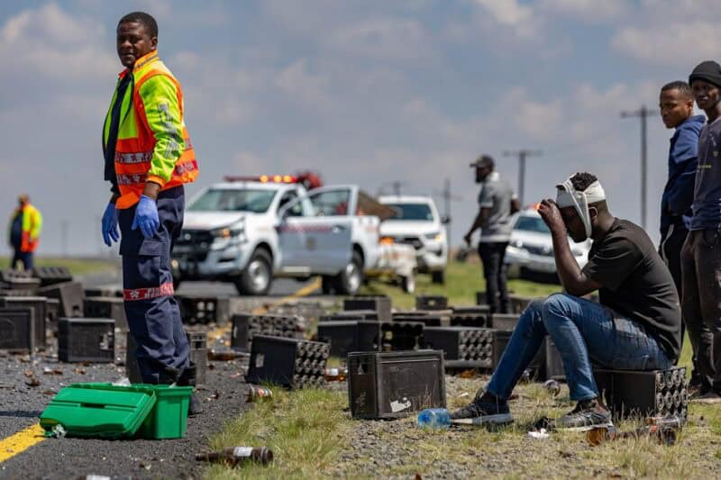 Injured driver sits beside the road with a bandaged head after a bakkie and trailer overturned.