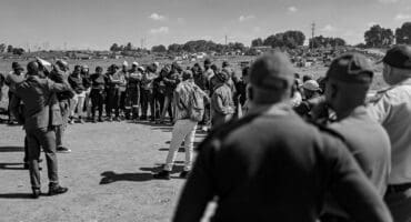 People gather under police observation near the Mpumalanga Stadium in Wesselton.