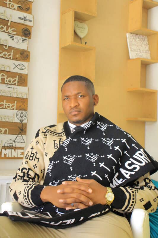 Siphamandla Nkosi seated indoors wearing a cream and black patterned outfit.