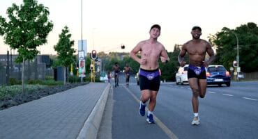 Two smiling runners wearing purple Daredevil speedos over black shorts run in Ermelo.