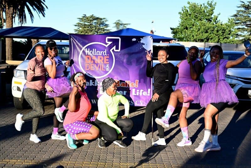 Seven women pose beside a purple Hollard Daredevil Run banner in Ermelo.