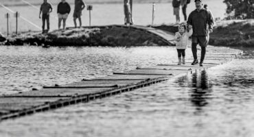 An older man holds a young girl's hand as they cross the Bull Run water bridge at the Glen Aggy Trail Run.