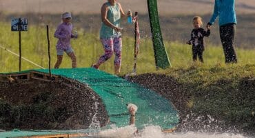 A trail runner splashes into water while tackling the Bull Run obstacle at Glen Aggy. Title: Runner makes a splash at Glen Aggy's Bull Run