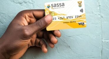 A hand holding a SASSA card, with text announcing new November payment dates.