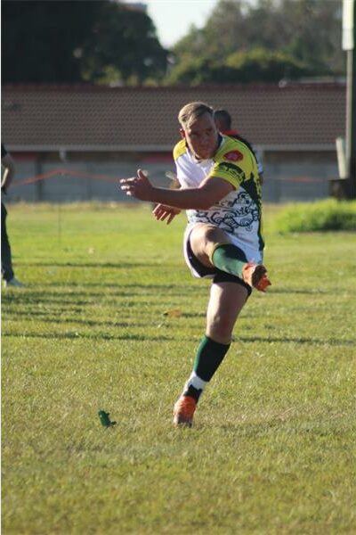 A man in a yellow and green jersey kicking a soccer ball.