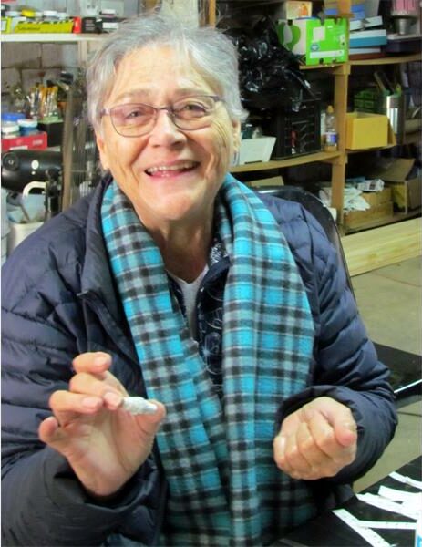 An older woman with glasses and a scarf smiles at the camera.