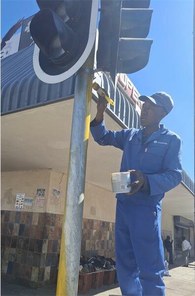 A man in blue overalls is fixing a traffic light.