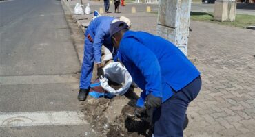 Two men are working on a street with a trash bag.