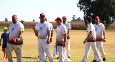 A group of men in white shirts and red hats playing cricket.